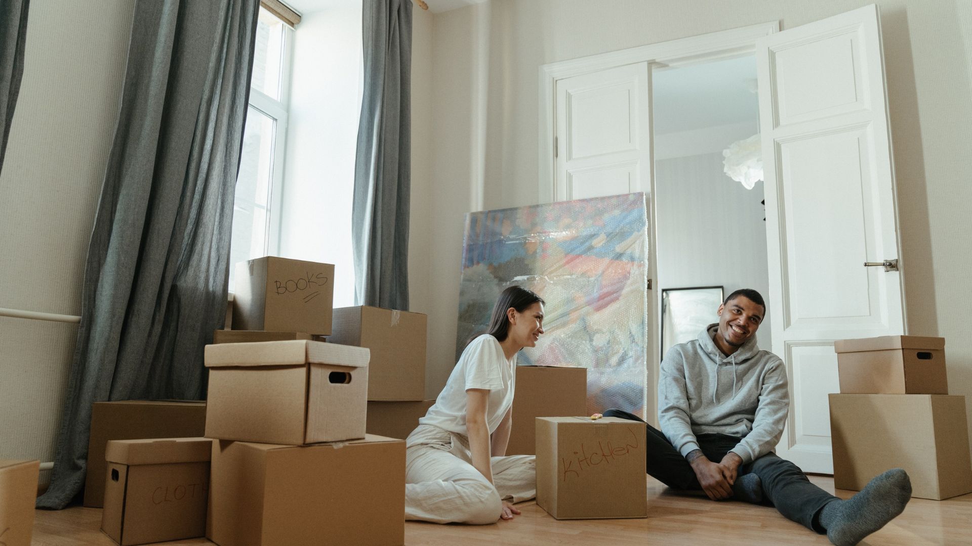 Happy couple celebrating after buying their first home in Canada, surrounded by moving boxes in their new living room