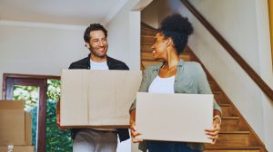 Happy couple celebrating after buying their first home in Canada, surrounded by moving boxes in their new living room.